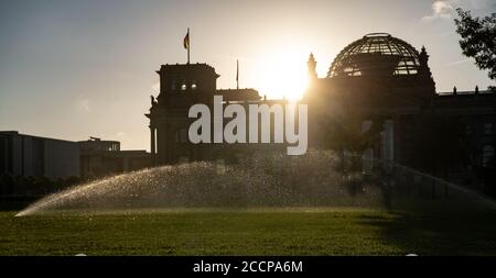 Berlin, Deutschland. August 2020. Das Wasser der Rasensprenger vor dem Reichstag leuchtet im Licht der aufgehenden Sonne. Quelle: Paul Zinken/dpa-Zentralbild/dpa/Alamy Live News Stockfoto