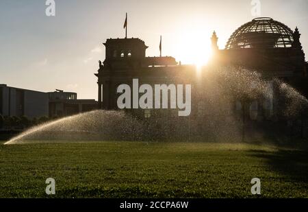 Berlin, Deutschland. August 2020. Das Wasser der Rasensprenger vor dem Reichstag leuchtet im Licht der aufgehenden Sonne. Quelle: Paul Zinken/dpa-Zentralbild/dpa/Alamy Live News Stockfoto