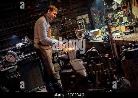 Der Schmied schmiedet das rotglühende Metall manuell auf dem Amboss In Schmiede mit Funkenfeuerwerk Stockfoto