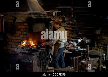 Schmied arbeitet mit offenem Feuer im Ofen. Der Schmied schmiedet heißes Eisen in der Werkstatt Stockfoto