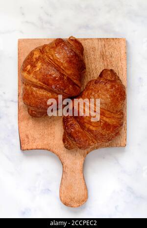 Frisch gebackene hausgemachte Croissants auf einem Holzbrett auf Marmor Hintergrund. Traditionelles Frühstück. Selektiver Fokus, Draufsicht Stockfoto