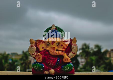 Hölzerne bunte Miniatur lord ganesha Idol mit verschwommenem bewölktem Himmel Und Baumhintergrund Stockfoto