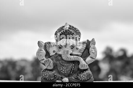 Schwarz und Weiß hölzerne bunte Miniatur lord ganesha Idol mit Verschwommener Himmel und Baumhintergrund Stockfoto