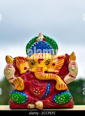 Hölzerne bunte Miniatur lord ganesha Idol mit verschwommenem Himmel und Baumhintergrund Stockfoto