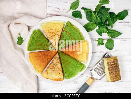 Verschiedene bunte Pfannkuchen. Weizen, Käse und Spinat Crepes in einem weißen Teller auf einem hölzernen Hintergrund. Selektiver Fokus, Draufsicht Stockfoto