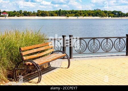 Park Holzbank auf dem gepflasterten Bürgersteig des Dnipro Böschung vor der Kulisse einer Sommerlandschaft und ein Sandstrand auf der anderen Flussseite in Ky Stockfoto