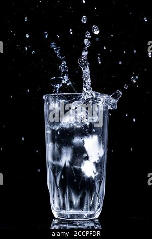 High-Speed-Fotografie von Eis spritzt in einem Glas Wasser auf schwarzem Hintergrund Stockfoto