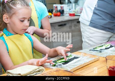 Das kleine Mädchen in der Schürze bereitet Sushi vor, das Gurken legt Stockfoto