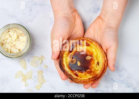 Eiertarte, traditionelles portugiesisches Dessert, Pastell de nata in den Händen. Portugiesischer Blätterteig mit Mandelblättern. Selektiver Fokus Stockfoto