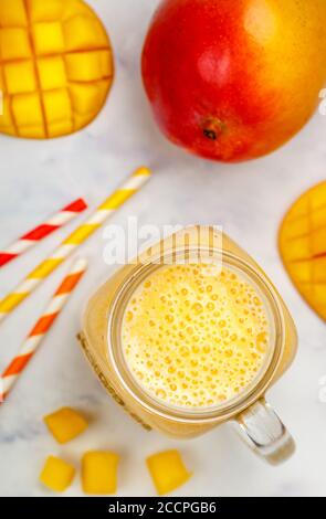 Smoothie oder Milchshake aus frischer Mango, Joghurt oder Milch und Eiswürfeln im Mason-Glas auf einem Marmortisch. Konzept der gesunden Vitamingetränke. Selektiv Stockfoto