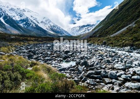 Neuseelands höchster Berg, Mount Cook, ist kaum sichtbar hinter weißen Wolken. Ein türkisfarbener Gletscherfluss fließt durch viele kleine Felsen. Stockfoto