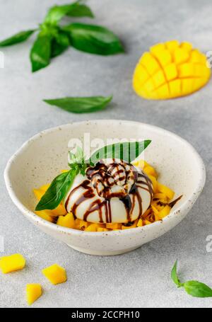 Feinkostkäse Burrata mit Mango-Tartare mit grünem Basilikum und Balsamico auf weißem Teller auf grauem Betongrund. Frühstück. Köstliche App Stockfoto