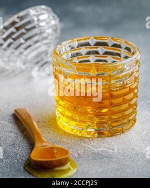 Flüssiger Blütenhonig in einem Glas mit Holzhonigtaube auf Beton- oder Steingrund. Selektiver Fokus Stockfoto