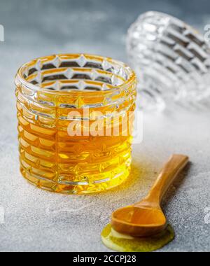 Flüssiger Blütenhonig in einem Glas mit Holzhonigtaube auf Beton- oder Steingrund. Selektiver Fokus Stockfoto
