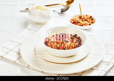 Hafergranola mit getrockneten Himbeeren, Heidelbeeren und Nüssen in einer weißen Schale auf einem Holztisch, Landschaftsansicht von oben, Nahaufnahme Stockfoto