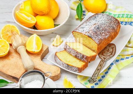Scheiben veganer glutenfreier Citrus-Kuchen-Laib mit Puderzucker auf einem weißen Teller auf hellem Holzhintergrund. Ein köstliches Leckerbissen für Tee oder Kaffee. S Stockfoto