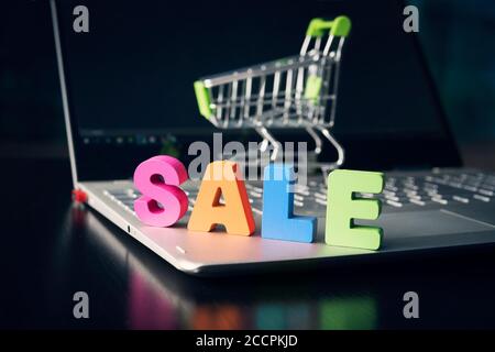 Nahaufnahme der großen farbigen Buchstaben VERKAUF auf geöffneten Laptop unten am Warenkorb und schwarzen leeren Display-Hintergrund gesetzt. Konzept des Online-Einkaufs Stockfoto