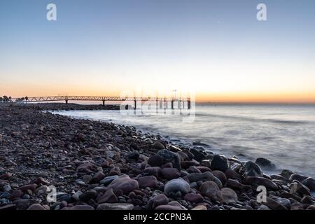 Sonnenaufgang von einem Kiesstrand mit einem Gehweg zum Meer Stockfoto