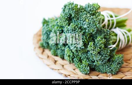 Bündel von rohen frischen Brokkolini auf einem Weidenstroh stehen auf einem weißen Hintergrund, vegetarisches Konzept Stockfoto