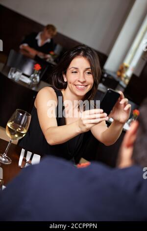 Frau fotografiert ihren Partner mit Handy im Restaurant Stockfoto