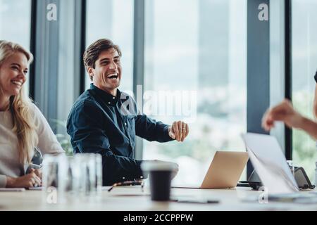 Fröhliche Geschäftsleute, die im Konferenzraum sitzen. Geschäftsmann und Frau lächeln während einer Besprechung im Büro. Stockfoto