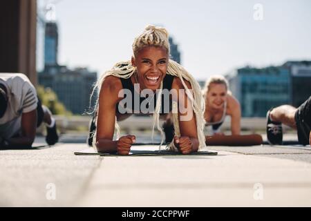 Gruppe junger Erwachsener, die draußen in der Stadt zusammen arbeiten. Männer und Frauen halten eine Plankenposition und lächeln. Stockfoto