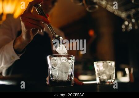 Der Barkeeper gießt Eis in Cocktailgläser. Stockfoto