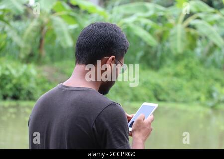 Junger Mann mit Smartphone und Blick auf den Handy-Bildschirm, von der Rückseite genommen Stockfoto