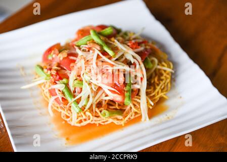 Papaya-Salat würzig auf knusprigen Nudeln auf weißem Teller, Thai-Essen mit langbohnenlangen Kräutern und Gewürzen Zutaten Chili Tomate Knoblauch Stockfoto