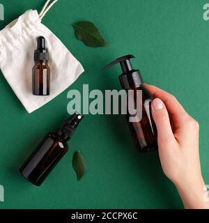 Weibliche Hand halten Pumpe Bernstein Glasflasche über grünem Hintergrund mit Sprühflasche und ätherisches Öl Tropfflasche. SPA natürliche organische Schönheit produ Stockfoto