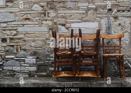 Stühle stapelten sich vor einer alten Steinmauer in Griechenland Stockfoto