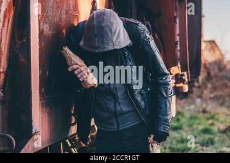Obdachlose Alkoholiker Alkohol neben alten Bahnhof wagen, betrunkener Mann mit Kapuze in Alkoholismus Konzept, selektiver Fokus Stockfoto