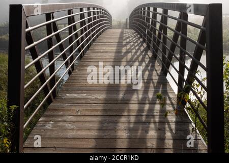 Holzfußbrücke mit Eisenstruktur im frühen Morgennebel Stockfoto