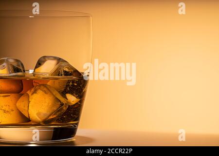 Glas Whiskey auf dem Eis aus der Nähe. Oder anderen Alkohol: Bourbon, Cognac oder Likör. Orangefarbener Hintergrund, freier Platz für Text, Kopierplatz. Stockfoto