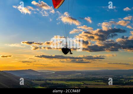 Gleitschirm, der gegen die untergehende Sonne und vereinzelte Wolken fliegt, über dem South Downs National Park. Brighton, East Sussex. Vereinigtes Königreich Stockfoto