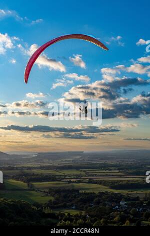 Gleitschirm, der gegen die untergehende Sonne und vereinzelte Wolken fliegt, über dem South Downs National Park. Brighton, East Sussex. Vereinigtes Königreich Stockfoto