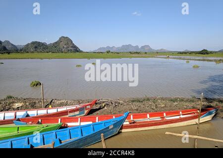 Burmesische ländliche Landschaft. Bunte Holzboote an einem See. Kalkstein Karst Berge und Hügel im Hintergrund. Myanmar, Burma, Südostasien Stockfoto