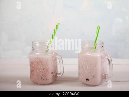 Zwei Gläser süßer Kirsch-Smoothies mit Strohhalmen auf weißem Holzhintergrund. Gesunde Ernährung Stockfoto