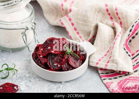 Gesunde Bio Purple Baked Beet (Rote Bete) Chips mit Olivenöl, großem Meersalz und Rosmarin in einer weißen Schüssel auf grauem Betongrund. Diätetisch Stockfoto