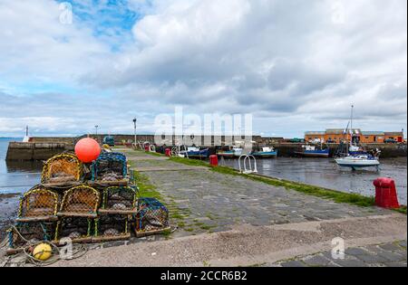 Cockenzie, East Lothian, Schottland, Großbritannien, 24. August 2020. Wetter in Großbritannien: Der Himmel erhellt sich im Hafen von Port Seton nach einem regnerischen Morgen mit Fischerbooten, die bei Ebbe im Schlamm liegen und einem Haufen Hummertöpfe oder Kreolen, die am Kai gestapelt sind Stockfoto