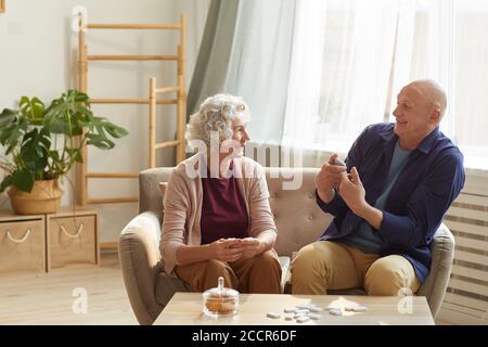 Warm getönte Porträt von glücklichen älteren Paar emotional reden, während auf der Couch sitzen in gemütlichen Innenraum von Sonnenlicht beleuchtet, kopieren Raum Stockfoto
