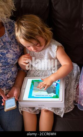 Kleines Kind weiblich 3 Jahre alt spielt auf einem Apfel IPad Air Computer mit ihrer Großmutter Foto von Simon gemacht Dack Stockfoto