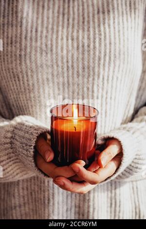 Frau in kuscheligen Pullover hält brennende Kerze Nahaufnahme. Gemütlicher Herbst oder Winter, Hygge Lifestyle Stockfoto