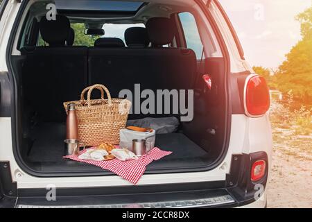 Picknick-Paket und Korb mit Croissant und Sandwiches liegt auf dem Kofferraum des Autos. Wochenende im Freien, Reisen vor Ort Stockfoto