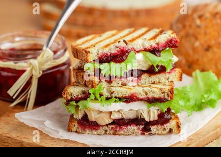 Köstliches Pute- oder Hühnerbrot mit Brie- oder Camembert-Käse, Salat und Preiselbeere (Preiselbeere, Preiselbeere) Chutney auf Getreidebrot mit Flachs siehe Stockfoto