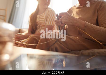 Warm getönte Nahaufnahme von unkenntlich Senior Frau Stricken mit niedlichen Mädchen beobachten sie in gemütlichen Haus durch Sonnenlicht beleuchtet, kopieren Raum Stockfoto