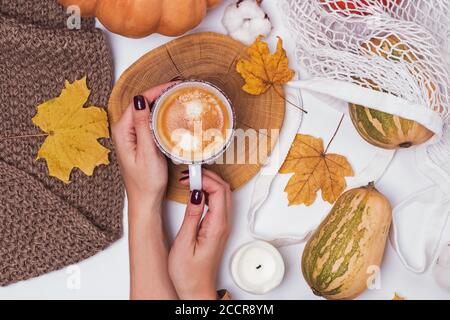 Herbstmorgen Kaffee Konzept. Flache Hände der Frau in der Hand Tasse Espresso auf weißem Hintergrund mit getrockneten gefallenen Blättern und Kürbissen halten Stockfoto