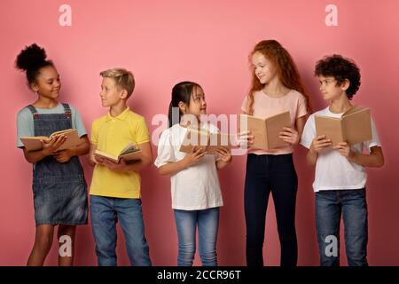 Portrait von niedlichen Mädchen und Jungen mit Schulbüchern suchen Aufeinander über rosa Hintergrund Stockfoto