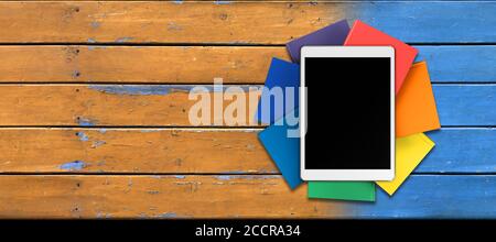 Tablet, Bücher in Regenbogenfarben auf dem Tisch von den alten Brettern, Vorderansicht Stockfoto