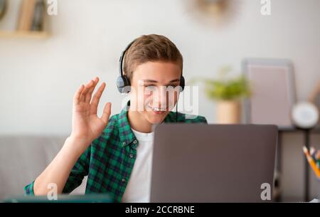 Fröhlicher Teenager, der eine Videokonferenz mit dem Lehrer hat und am Bildschirm winkt Stockfoto